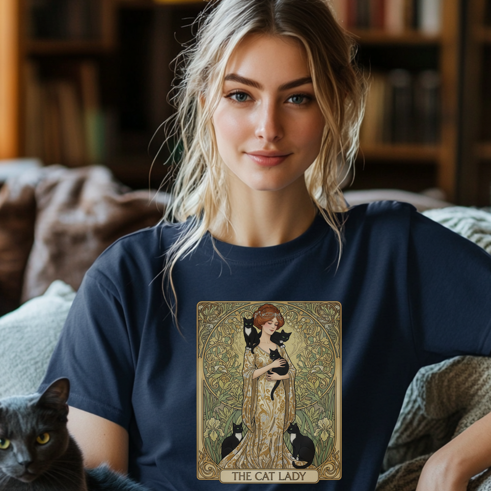 Woman wearing a t-shirt with a cat-themed design, sitting on a couch with two cats and books.