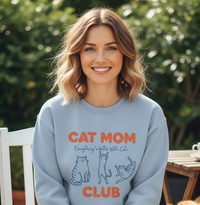 Load image into Gallery viewer, Woman wearing a light blue sweatshirt with &#39;Cat Mom Club&#39; text and cat illustrations outdoors.
